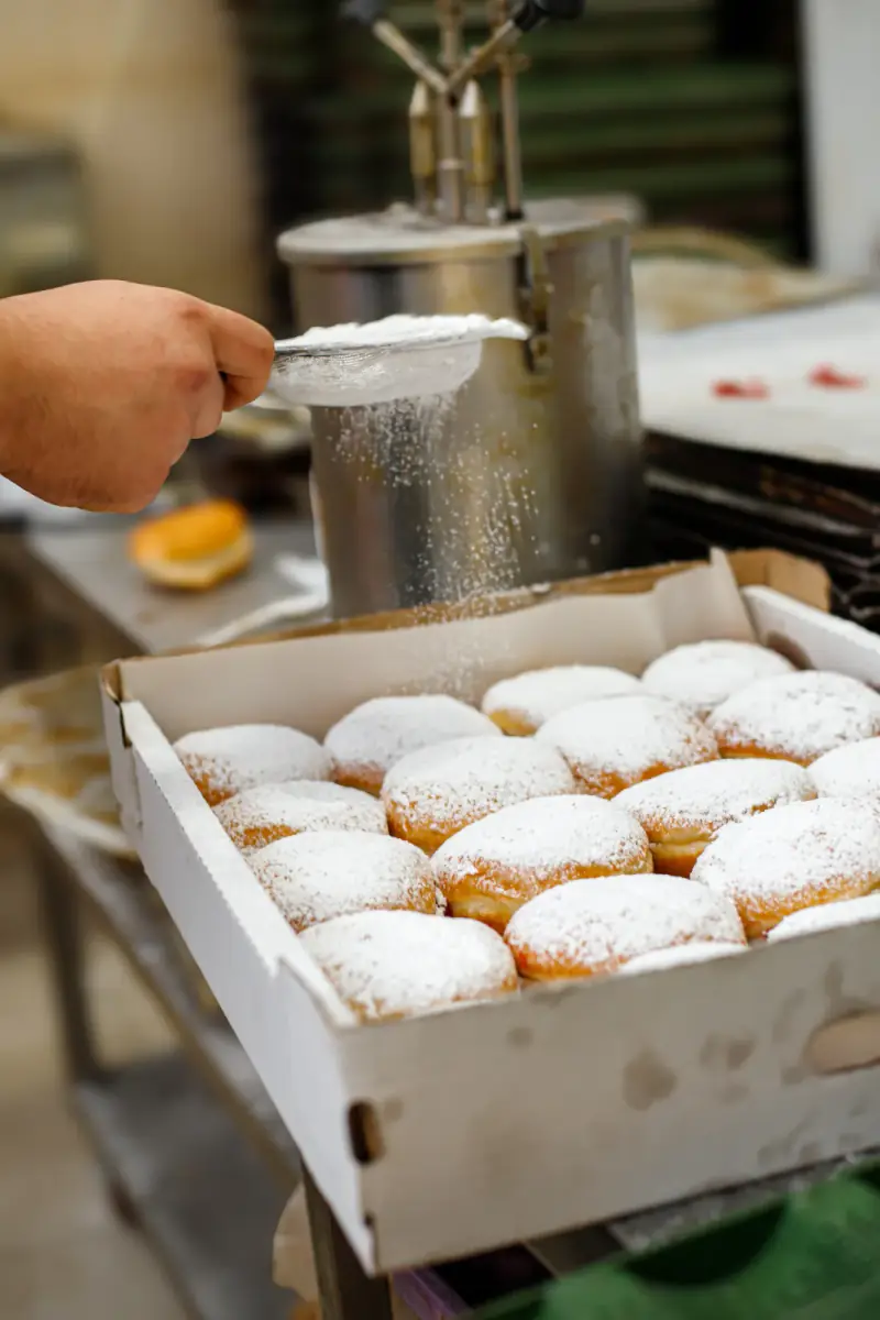Bakker strooit poedersuiker over vers gebakken oliebollen